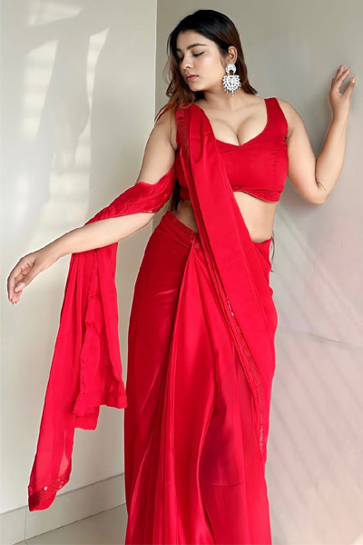 Stylish woman wearing a bright red saree near a wall.