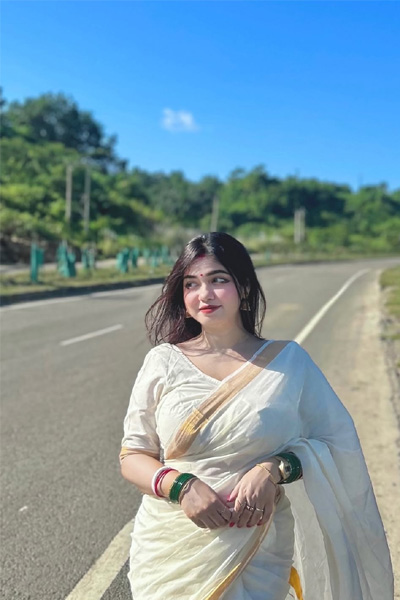 Woman in a traditional saree posing confidently under blue sky.