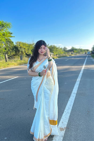 Stylish woman wearing a white saree with gold border outdoors.