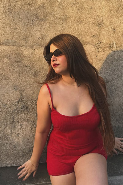 Confident woman dressed in red, standing near a concrete background.