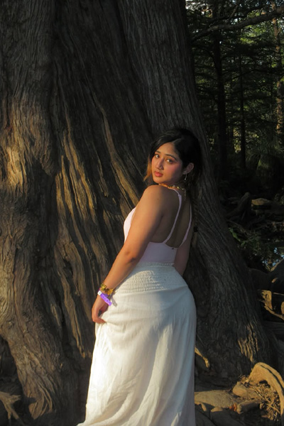 Confident woman posing in nature surrounded by greenery and trees.