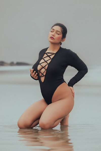 Stylish woman in black beachwear standing near ocean waves.