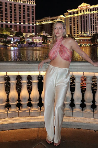 Woman posing stylishly by a city waterfront at night wearing a trendy halter top and satin pants